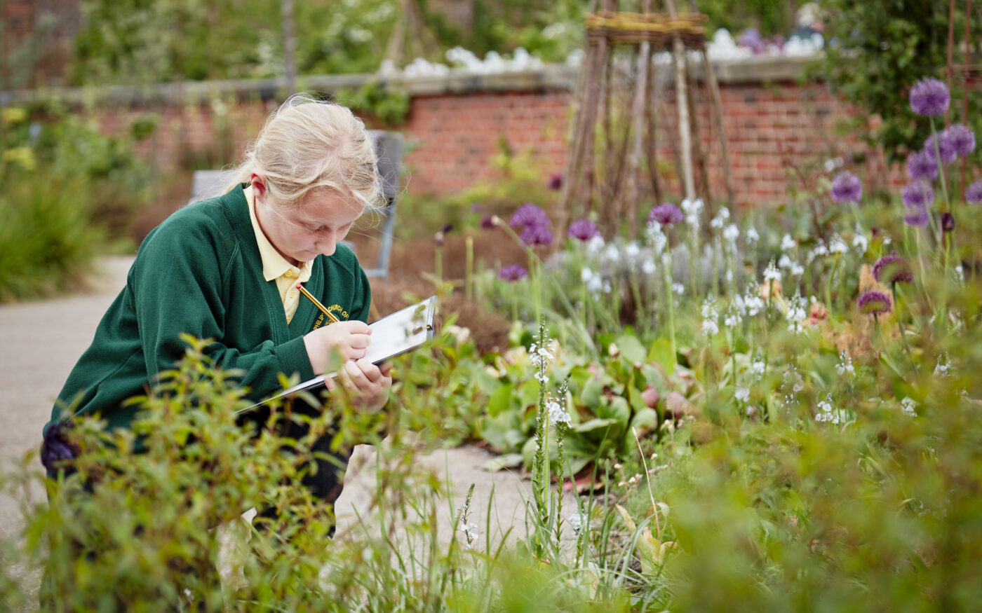 A school student among flowers in a garden writing on a clipboard