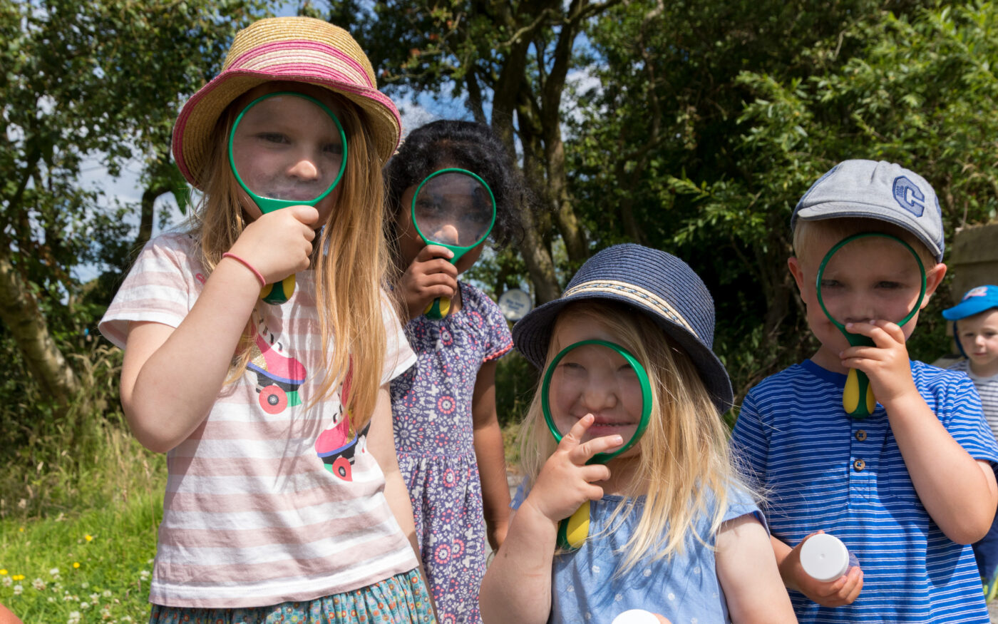 Children standing in a row holding magnifying glasses to their eyes.